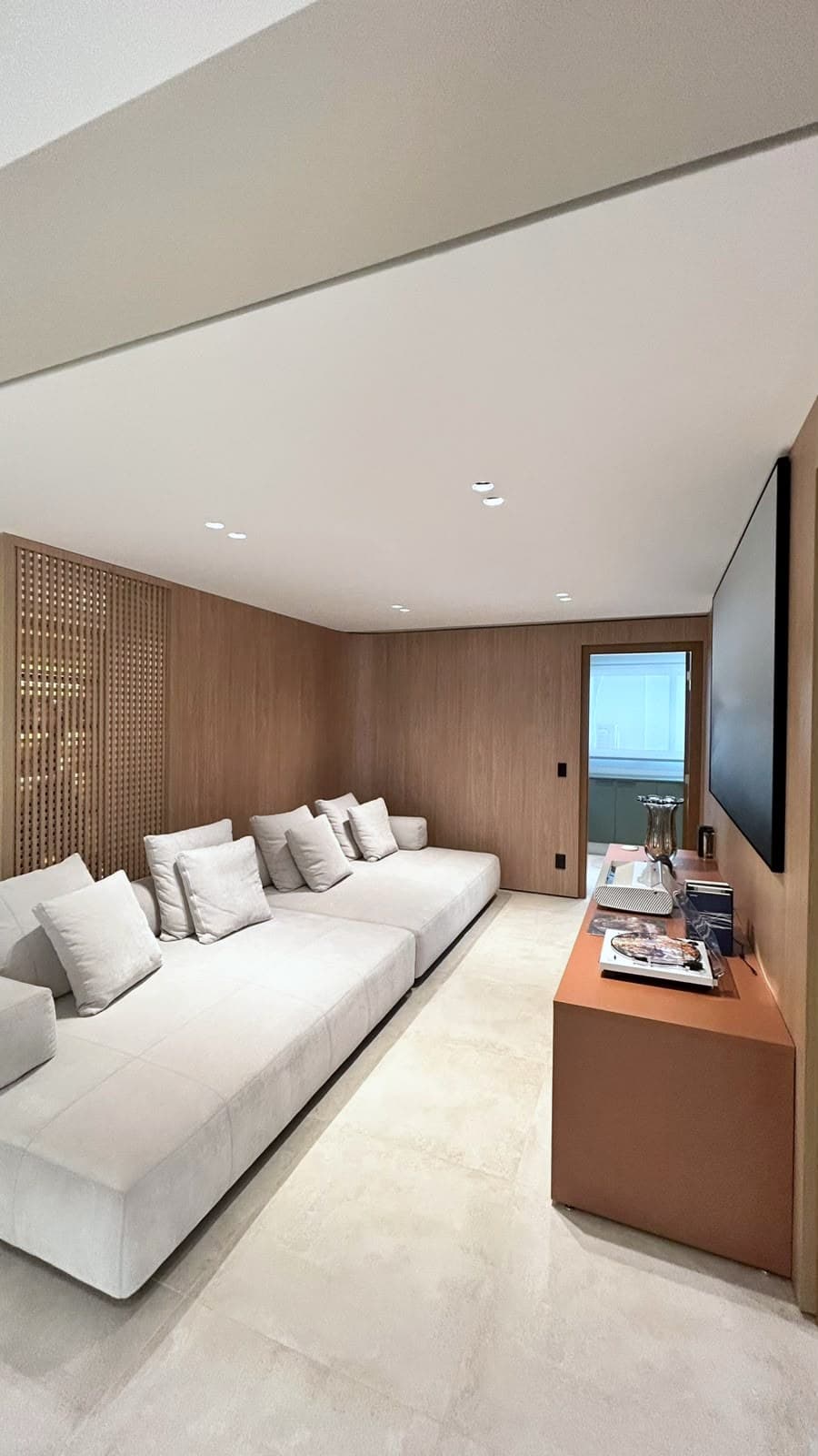 Living com sofá modular claro, painel de madeira e aparador terracota